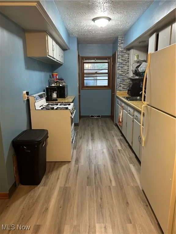 Kitchen with fridge, stove, light wood-style floors, light countertops, and a textured ceiling