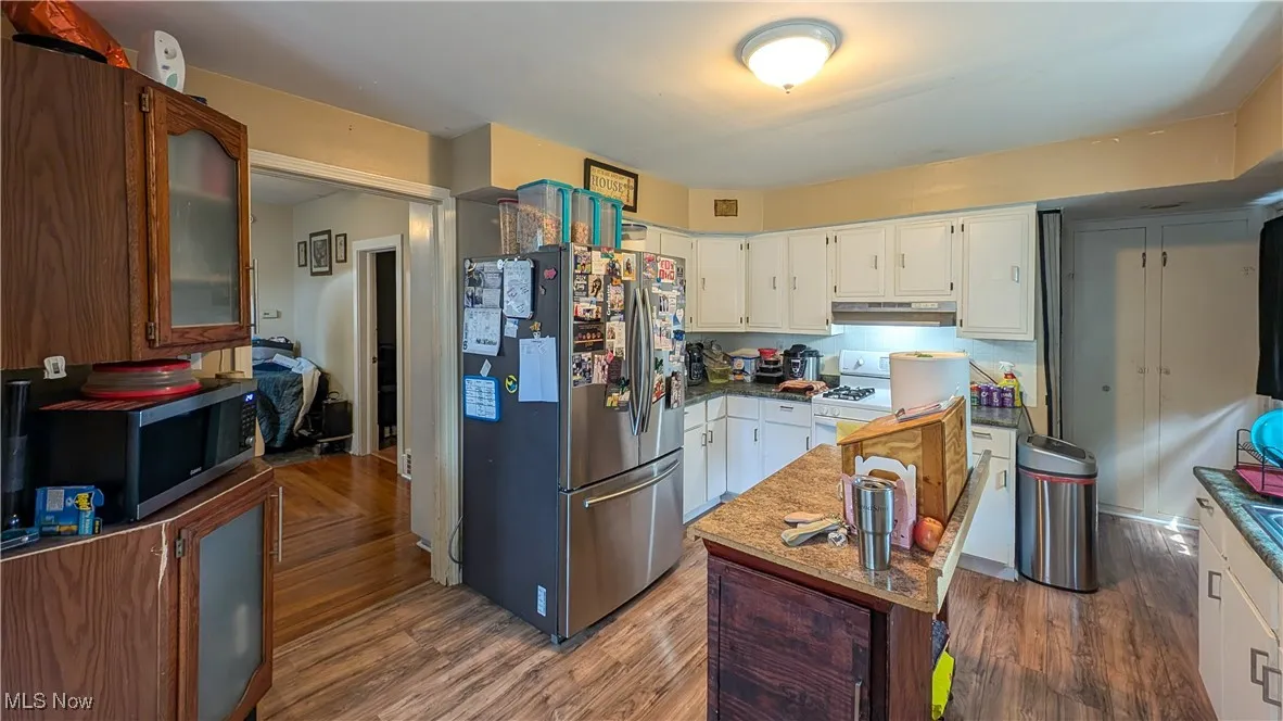 Kitchen with appliances with stainless steel finishes, under cabinet range hood, wood finished floors, a kitchen island, and glass insert cabinets