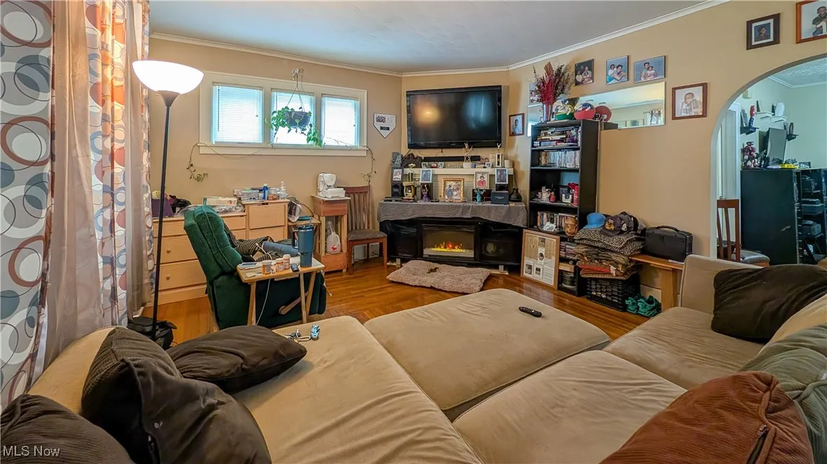 Living room featuring arched walkways, crown molding, wood finished floors, and a glass covered fireplace