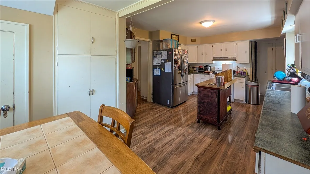 Kitchen featuring freestanding refrigerator, a center island, under cabinet range hood, dark wood finished floors, and dark countertops