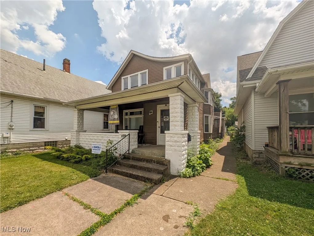 View of front of home with covered porch, a front yard, and stone siding
