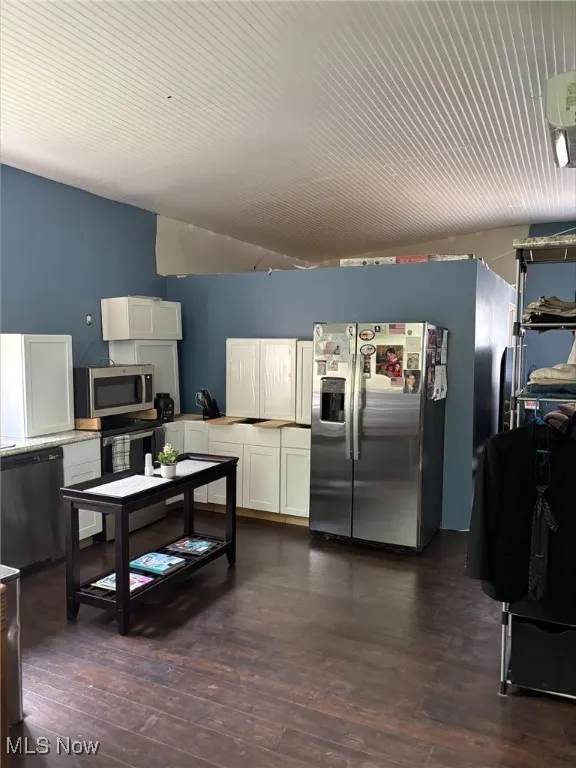 Kitchen with stainless steel appliances, white cabinetry, dark wood-style floors, light countertops, and wooden ceiling