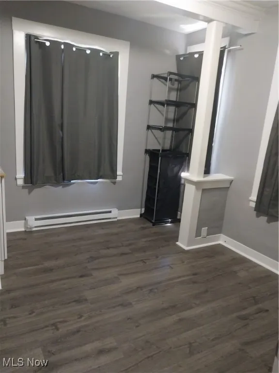 Unfurnished living room featuring a baseboard heating unit and dark wood finished floors