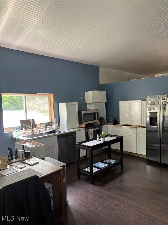 Kitchen with stainless steel appliances, lofted ceiling, dark wood finished floors, and white cabinets