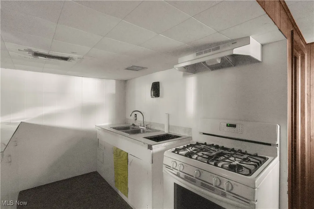 Kitchen featuring white range with gas cooktop, extractor fan, light countertops, and a drop ceiling
