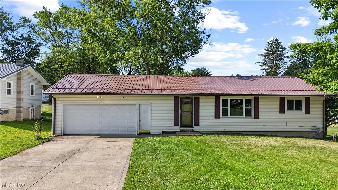 Single story home with driveway, an attached garage, a metal roof, and a front lawn