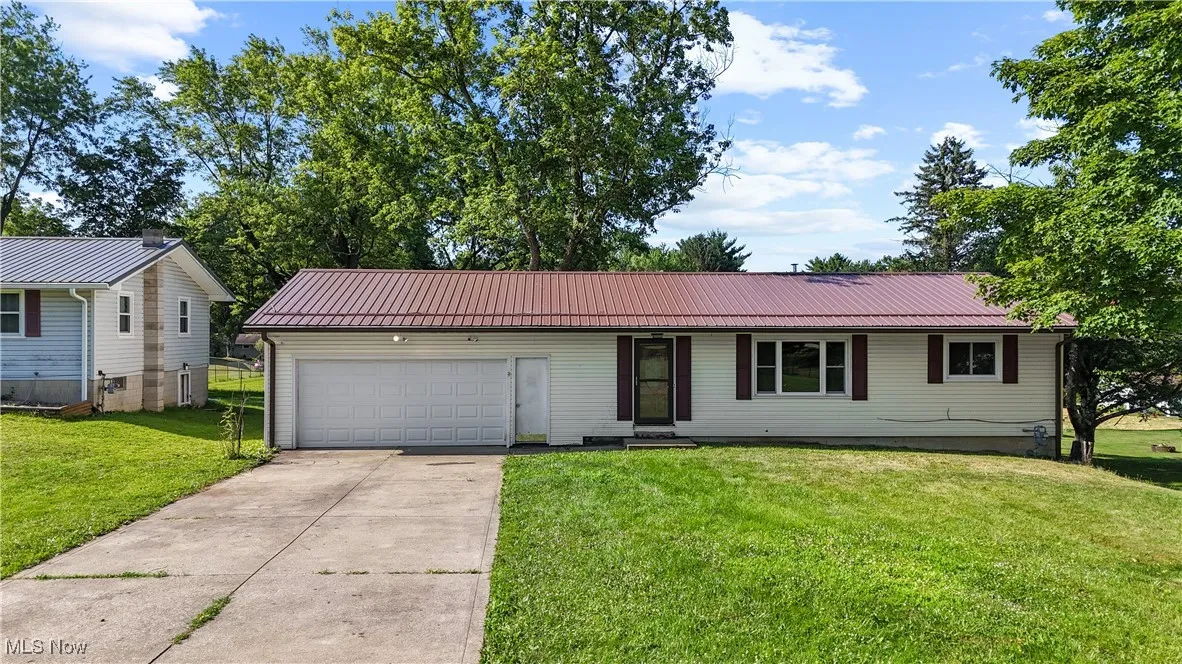 Ranch-style house featuring concrete driveway, a garage, a front lawn, and a metal roof