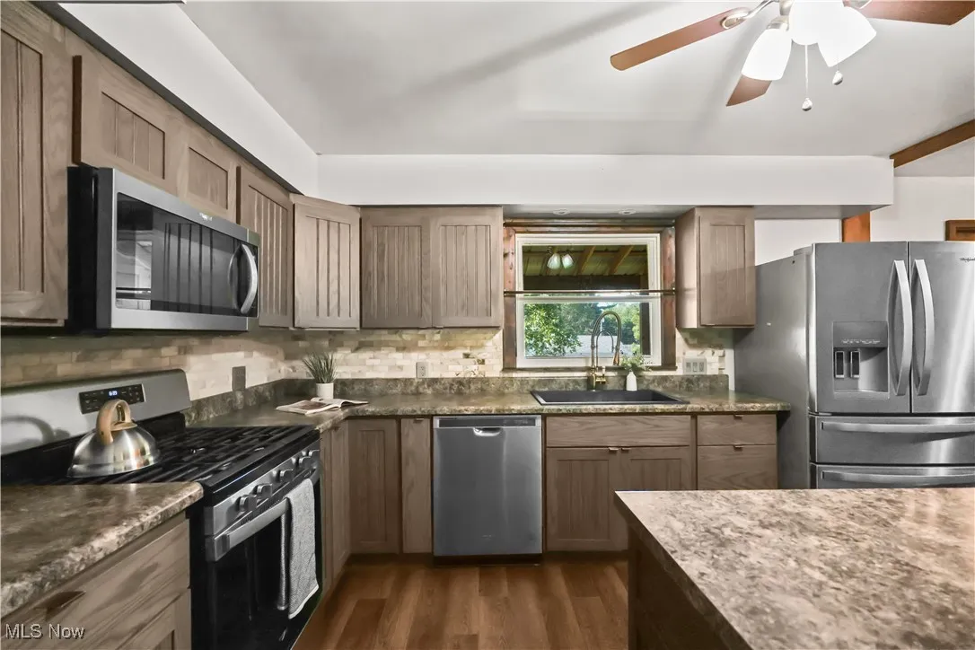 Kitchen featuring appliances with stainless steel finishes, dark wood-style floors, tasteful backsplash, and ceiling fan