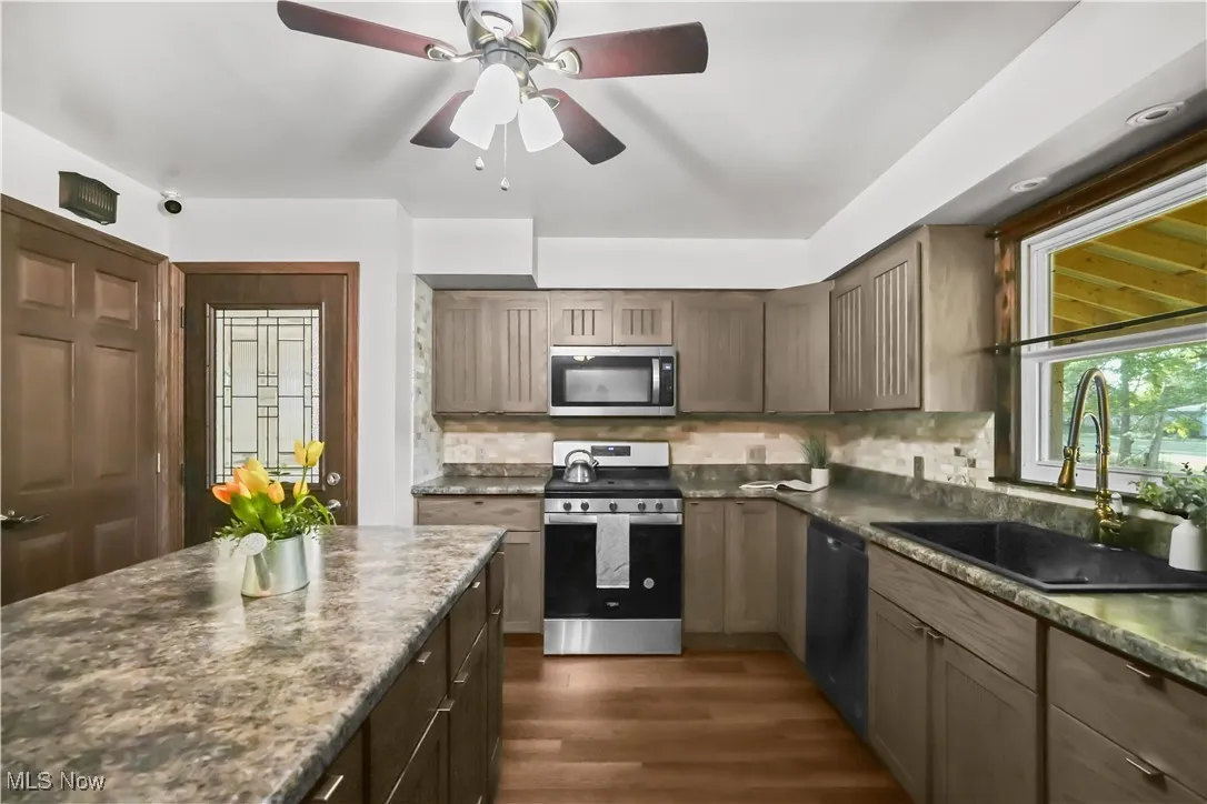 Kitchen featuring stainless steel appliances, tasteful backsplash, a ceiling fan, dark wood-type flooring, and dark stone countertops