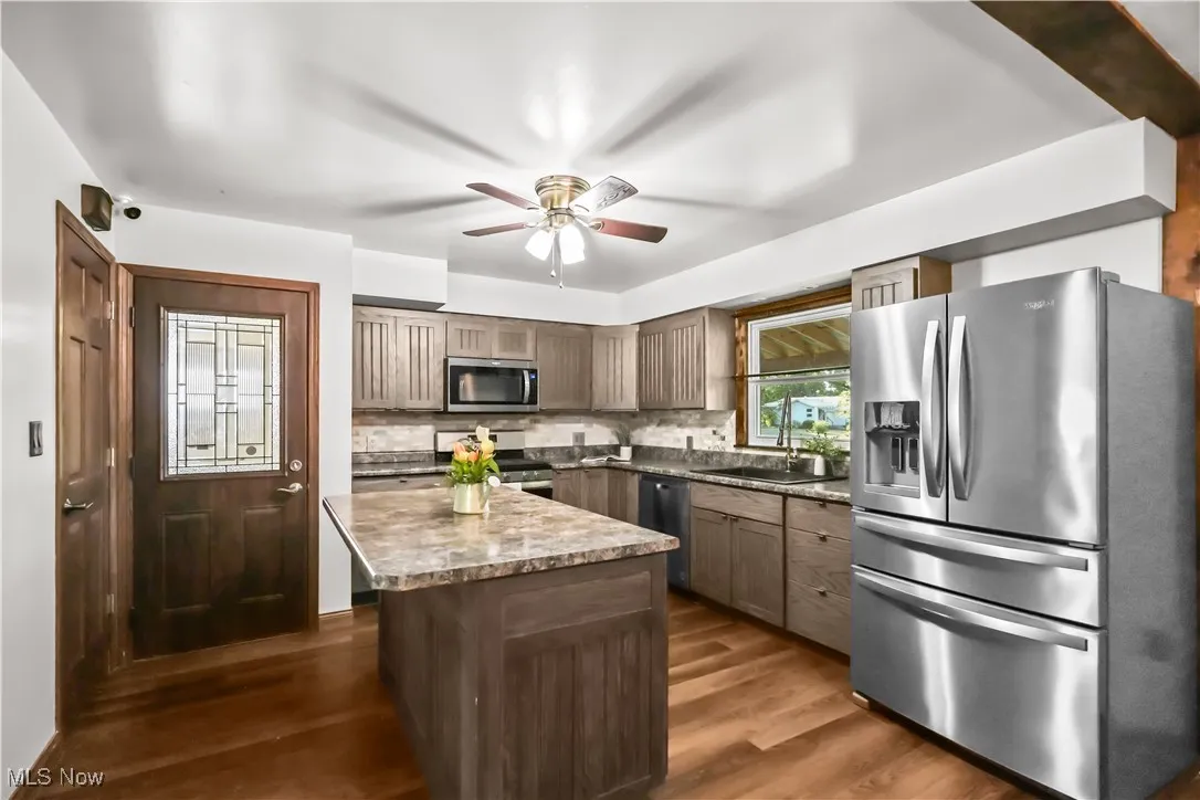 Kitchen featuring stainless steel appliances, ceiling fan, a kitchen island, tasteful backsplash, and dark wood finished floors