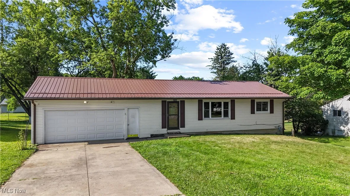 Single story home featuring concrete driveway, an attached garage, a metal roof, and a front yard