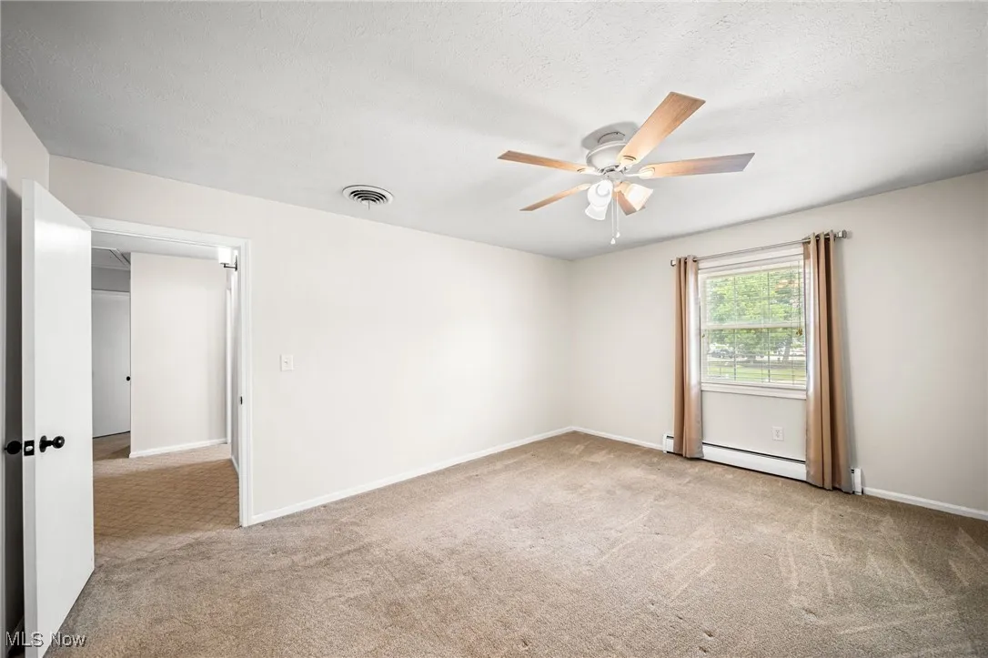 Carpeted spare room featuring a ceiling fan, a baseboard heating unit, and a textured ceiling