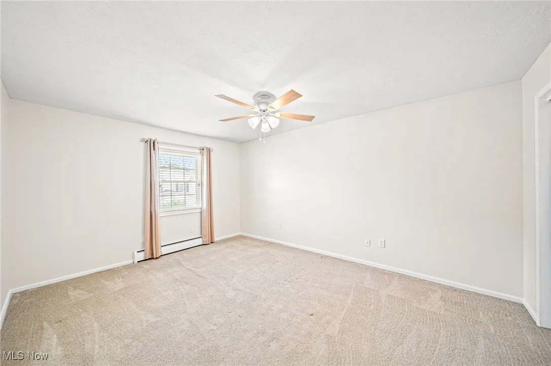 Empty room featuring ceiling fan, a baseboard heating unit, carpet, and a textured ceiling