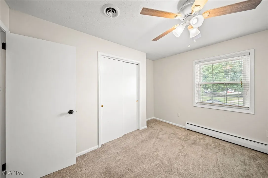 Unfurnished bedroom with baseboard heating, carpet, a closet, and ceiling fan