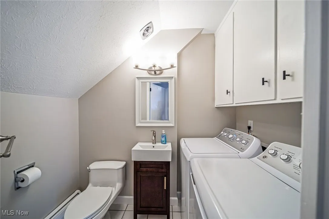 Bathroom featuring washing machine and clothes dryer, tile patterned flooring, a textured ceiling, vanity, and lofted ceiling