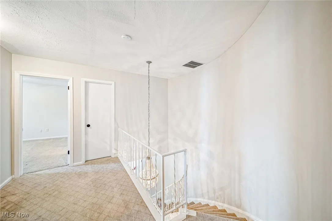 Corridor featuring an upstairs landing, carpet flooring, a chandelier, and a textured ceiling