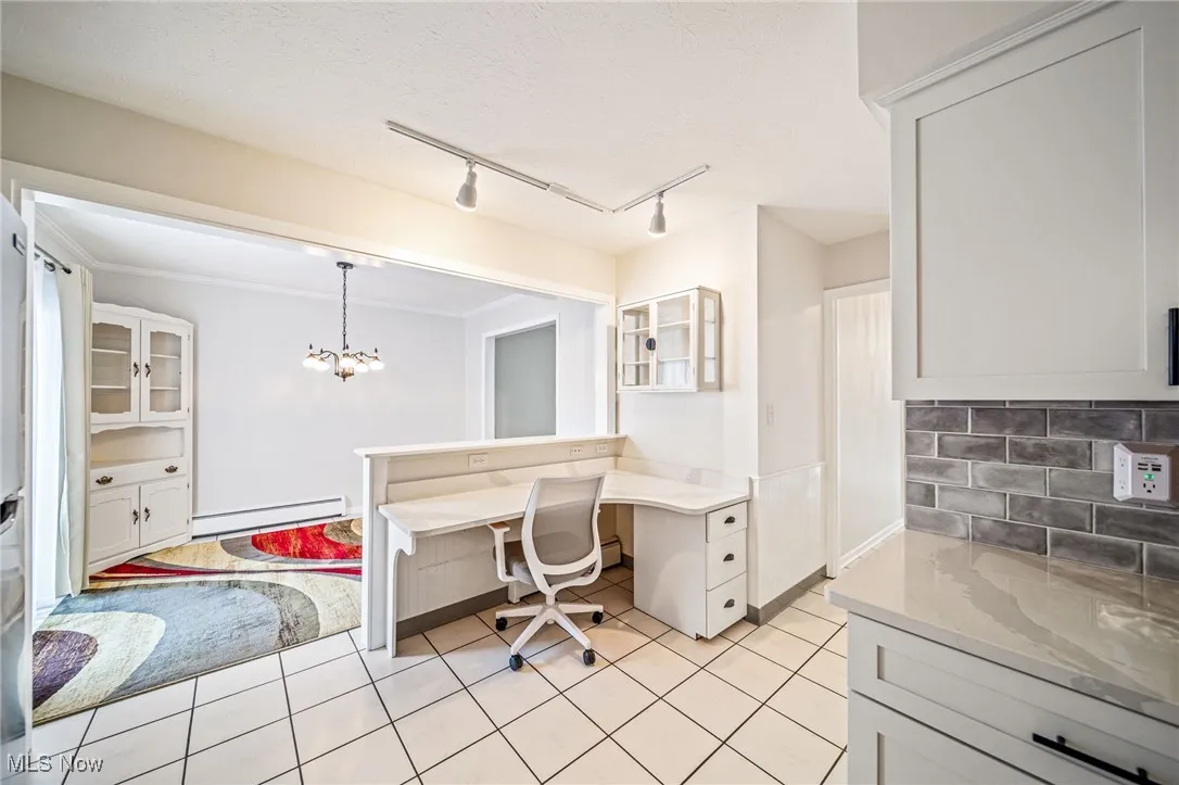 Kitchen featuring a baseboard heating unit, track lighting, decorative backsplash, glass insert cabinets, and light tile patterned floors