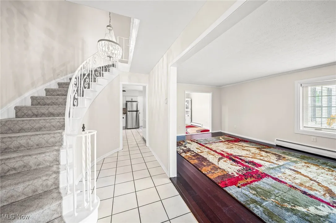 Tiled foyer featuring stairway, a baseboard heating unit, baseboard heating, and a chandelier