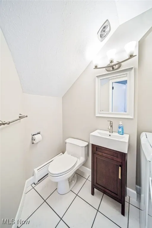 Half bath with a textured ceiling, vanity, vaulted ceiling, washer / clothes dryer, and tile patterned floors