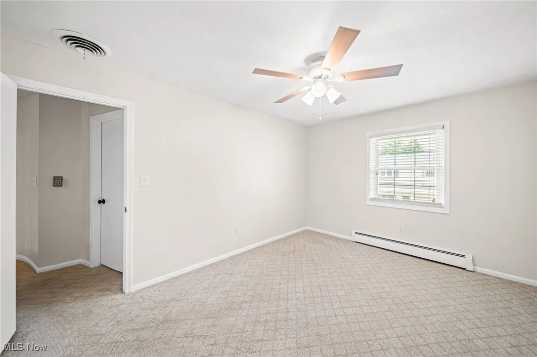 Carpeted empty room with baseboard heating and a ceiling fan