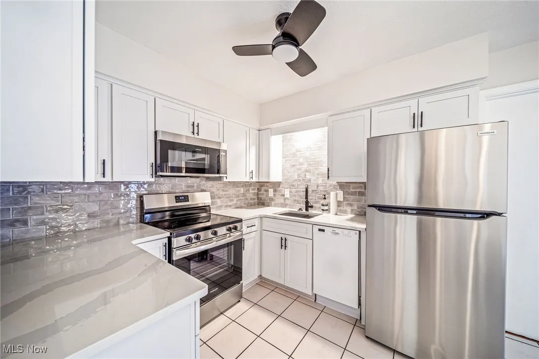 Kitchen featuring appliances with stainless steel finishes, a ceiling fan, white cabinets, decorative backsplash, and light stone countertops