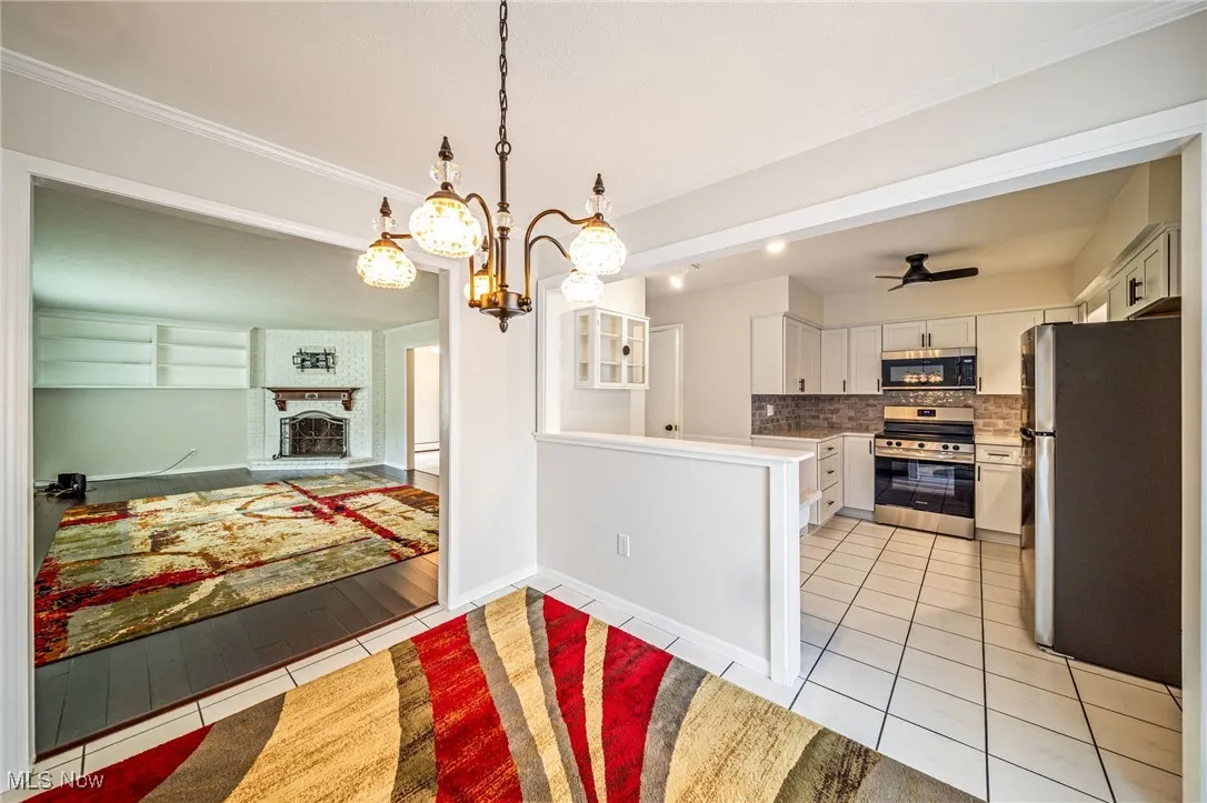 Kitchen featuring appliances with stainless steel finishes, light tile patterned flooring, backsplash, white cabinets, and light countertops
