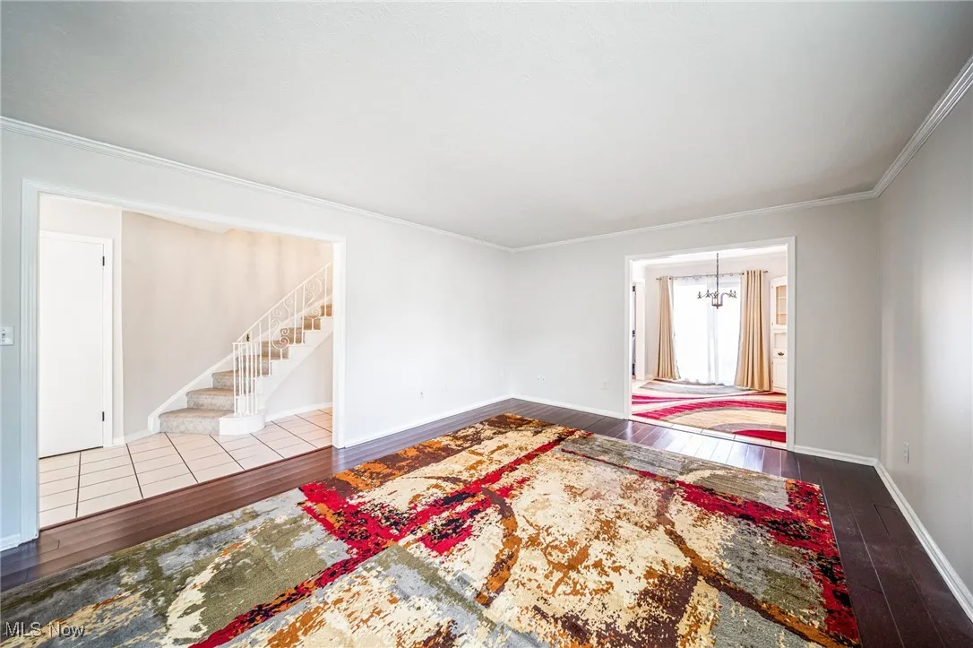 Empty room with a chandelier, hardwood / wood-style floors, stairs, and crown molding