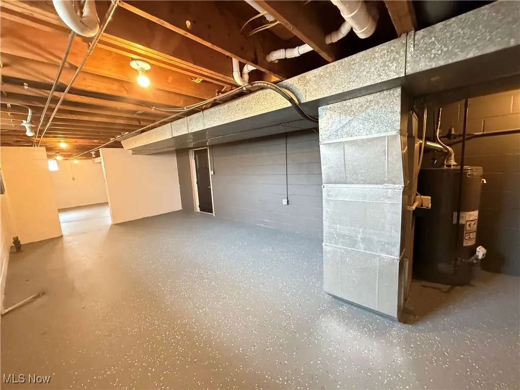 Unfinished below grade area with gas water heater, heating unit, and concrete block wall