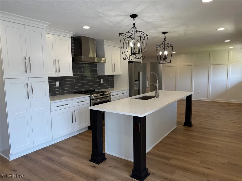 Kitchen with appliances with stainless steel finishes, wall chimney range hood, a breakfast bar, white cabinetry, and recessed lighting