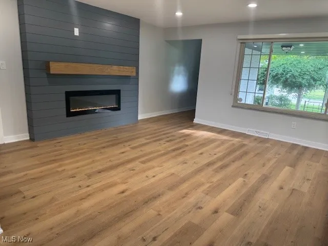 Unfurnished living room featuring wood finished floors, a large fireplace, and recessed lighting