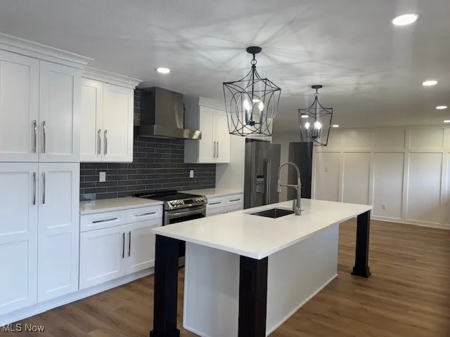 Kitchen featuring wall chimney range hood, appliances with stainless steel finishes, a breakfast bar area, white cabinetry, and tasteful backsplash