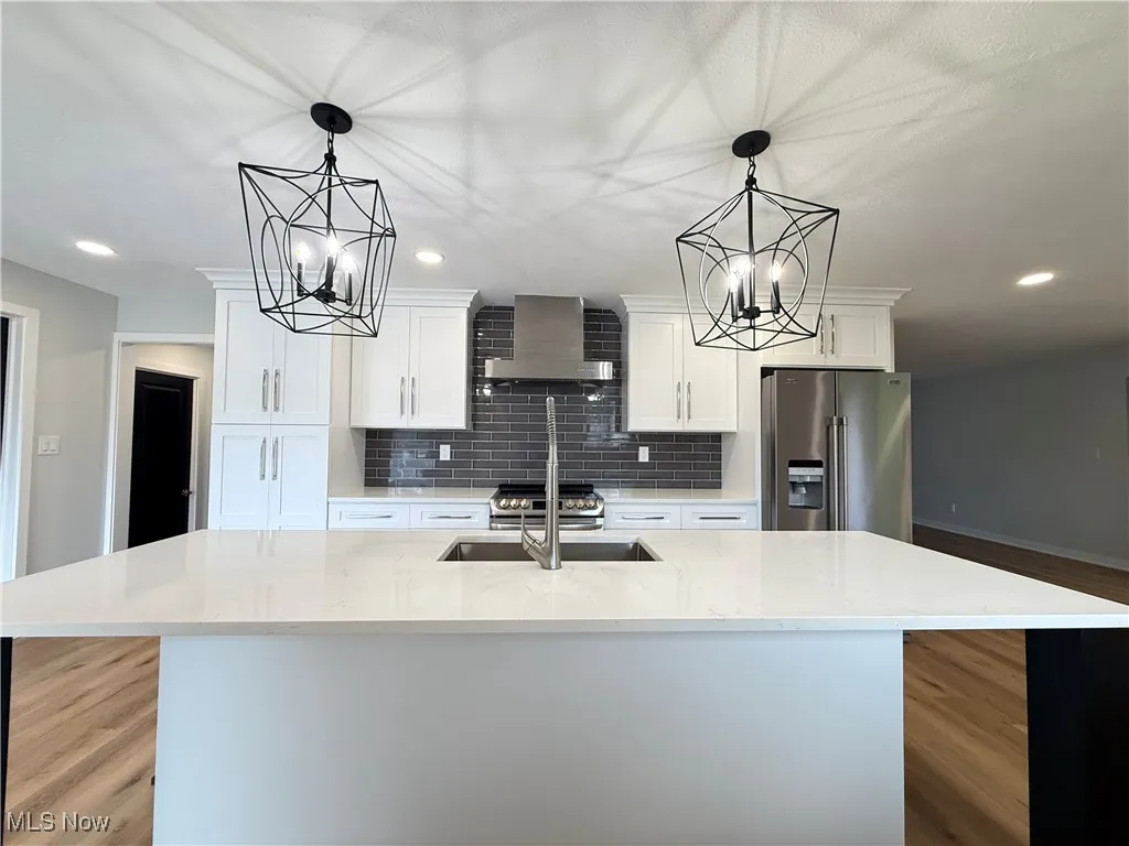 Kitchen with stainless steel refrigerator with ice dispenser, wall chimney exhaust hood, a chandelier, a center island with sink, and decorative backsplash