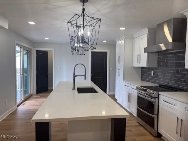 Kitchen with double oven range, wall chimney range hood, tasteful backsplash, a kitchen island with sink, and white cabinetry