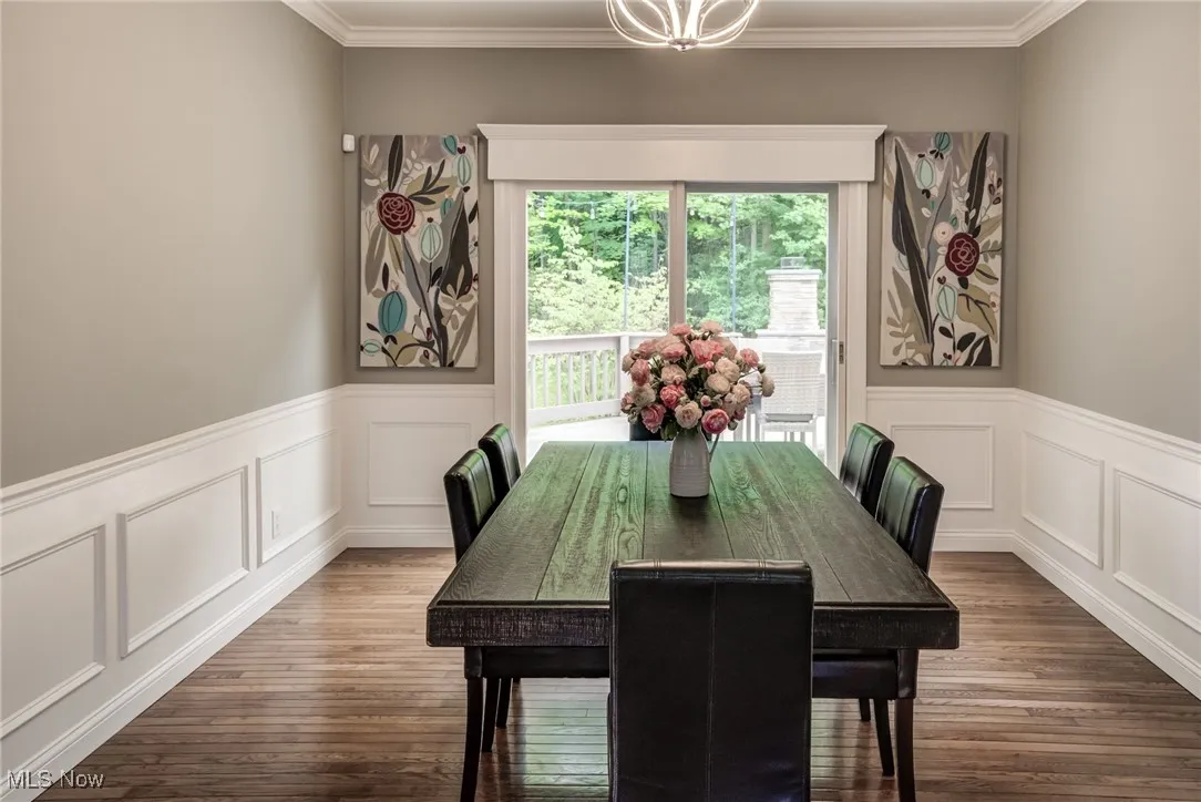Dining area featuring wood finished floors, crown molding, a decorative wall, and a wainscoted wall