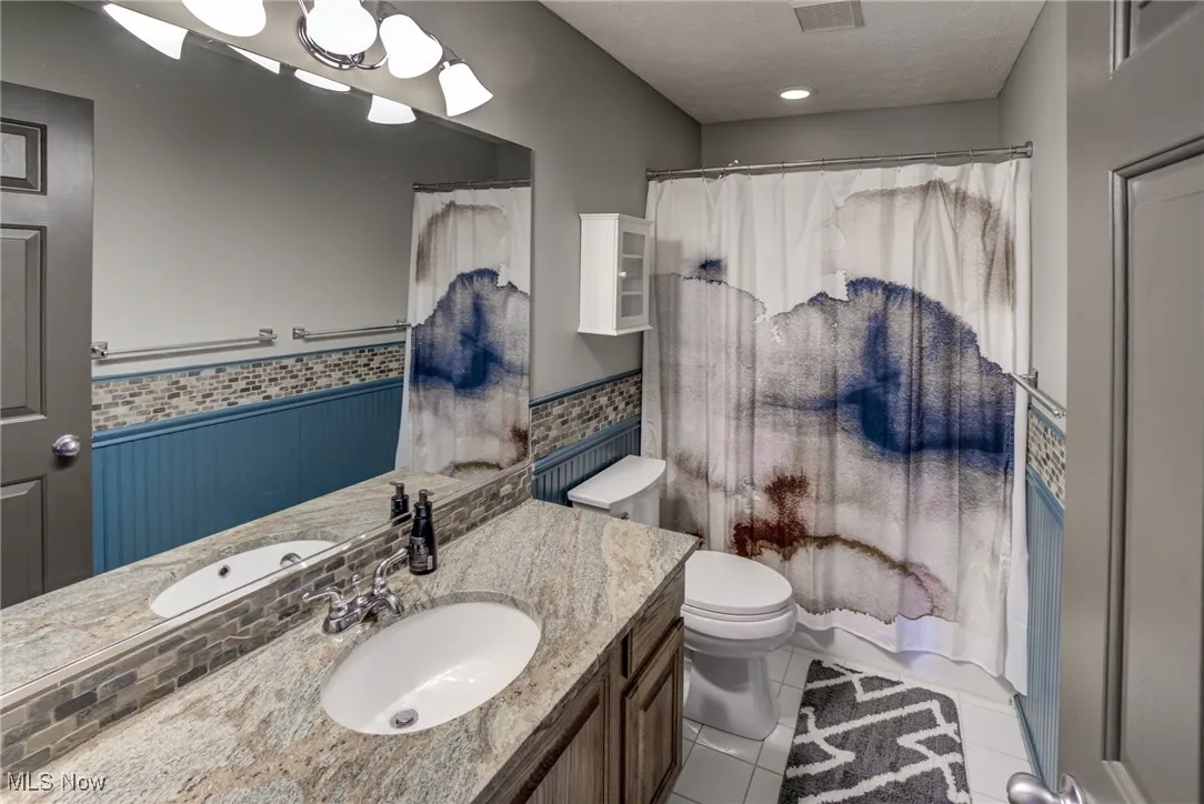 Bathroom featuring a wainscoted wall, vanity, tile patterned flooring, and a shower with shower curtain