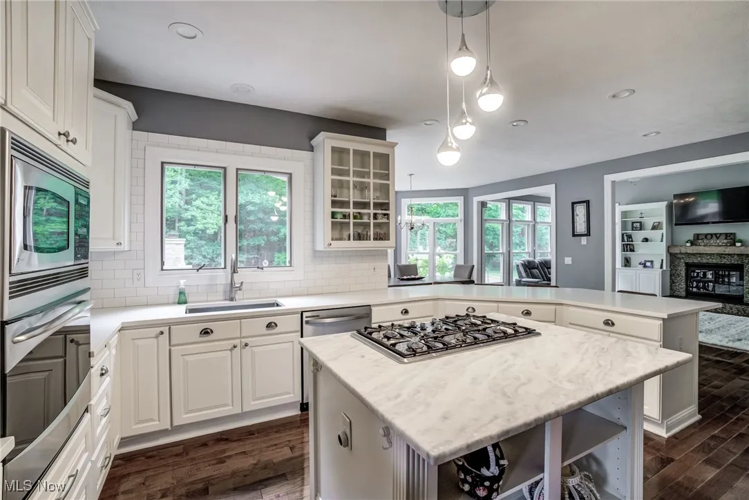 Kitchen featuring stainless steel appliances, dark wood-style floors, a peninsula, backsplash, and healthy amount of natural light