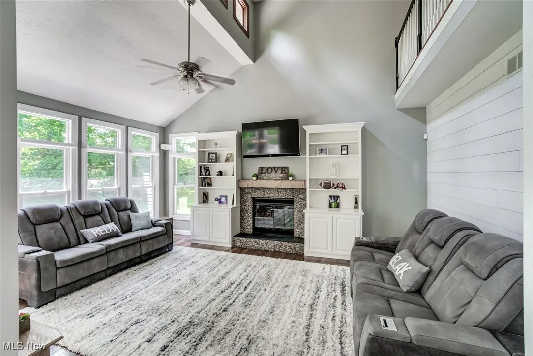 Living room with ceiling fan, wood finished floors, a glass covered fireplace, and high vaulted ceiling