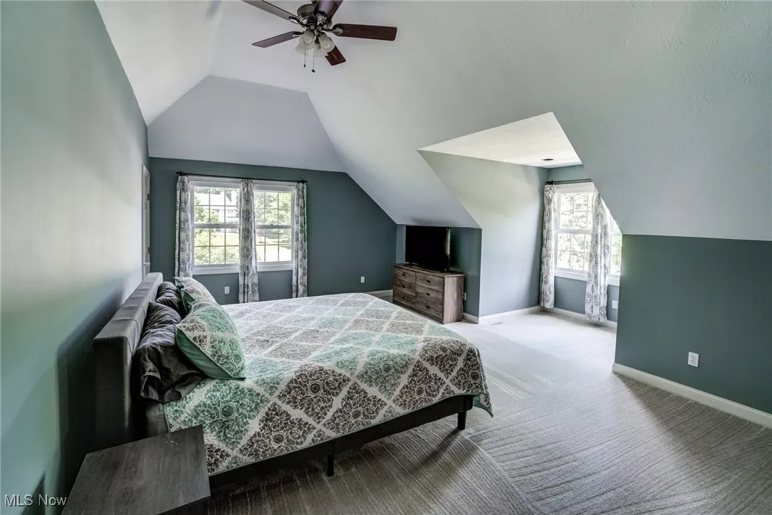 Carpeted bedroom with lofted ceiling, multiple windows, and ceiling fan