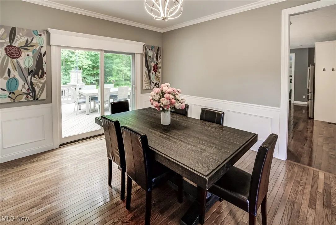 Dining area with a chandelier, light wood-style floors, a wainscoted wall, ornamental molding, and a decorative wall