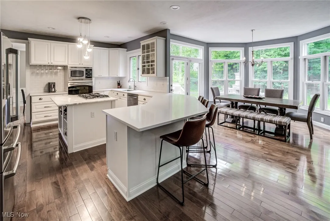 Kitchen featuring appliances with stainless steel finishes, a breakfast bar area, light countertops, dark wood-style floors, and decorative backsplash