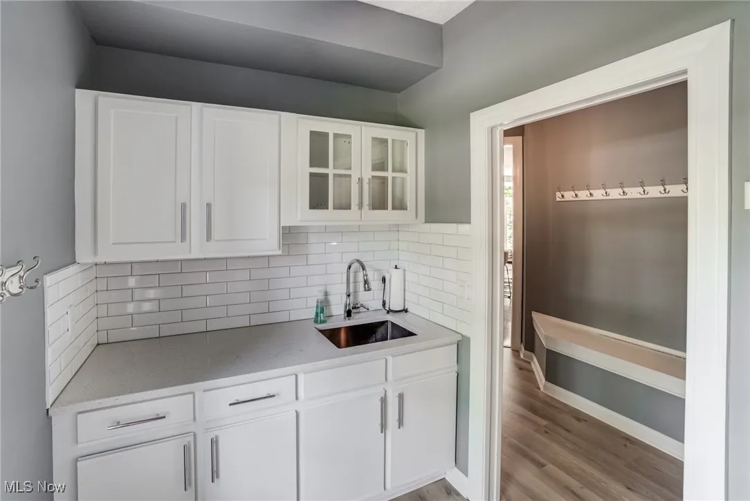 Kitchen featuring tasteful backsplash, light wood-style floors, glass insert cabinets, and white cabinets