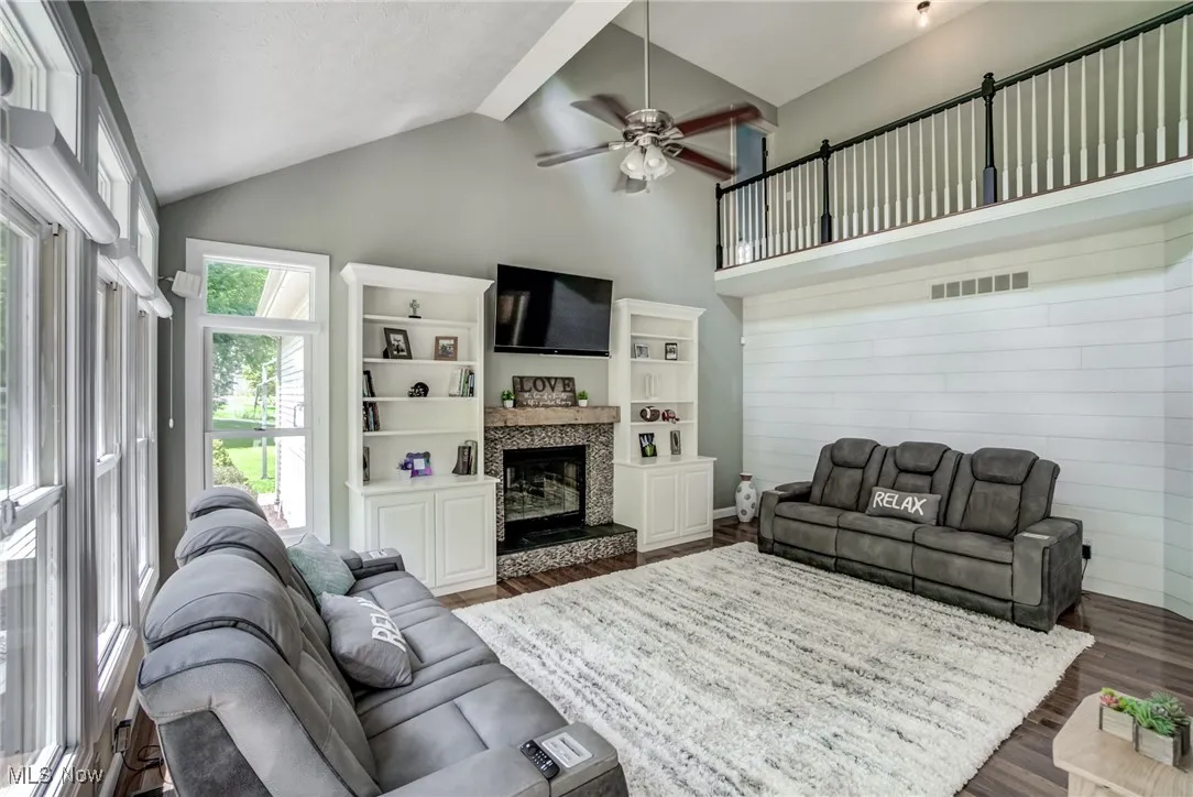 Living room with dark wood-style flooring, ceiling fan, vaulted ceiling, a glass covered fireplace, and wood walls