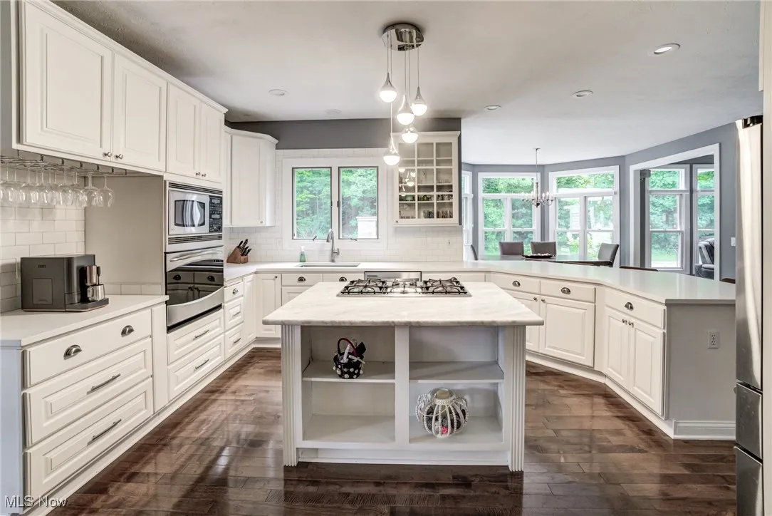 Kitchen with stainless steel appliances, a peninsula, open shelves, light countertops, and dark wood-type flooring