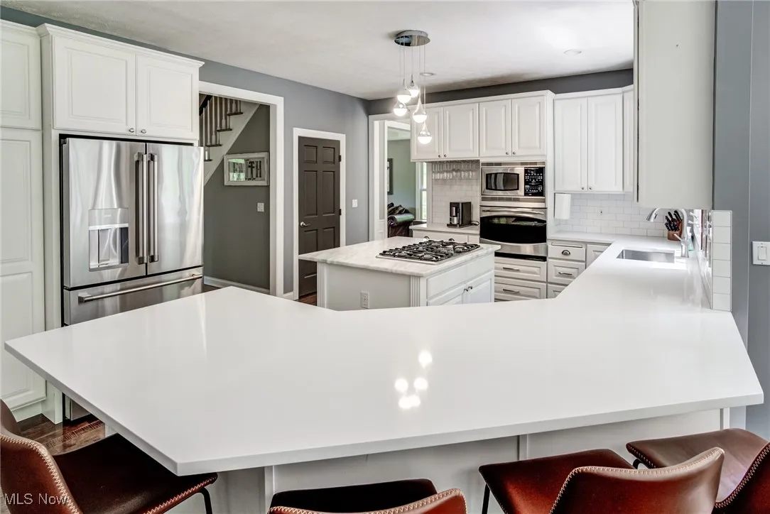 Kitchen with stainless steel appliances, decorative backsplash, a kitchen island, white cabinetry, and light countertops