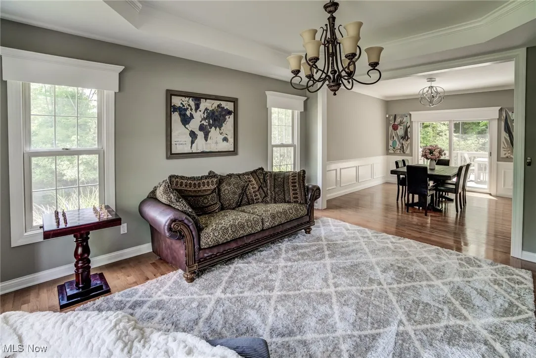 Living area with a chandelier, crown molding, wood finished floors, and wainscoting