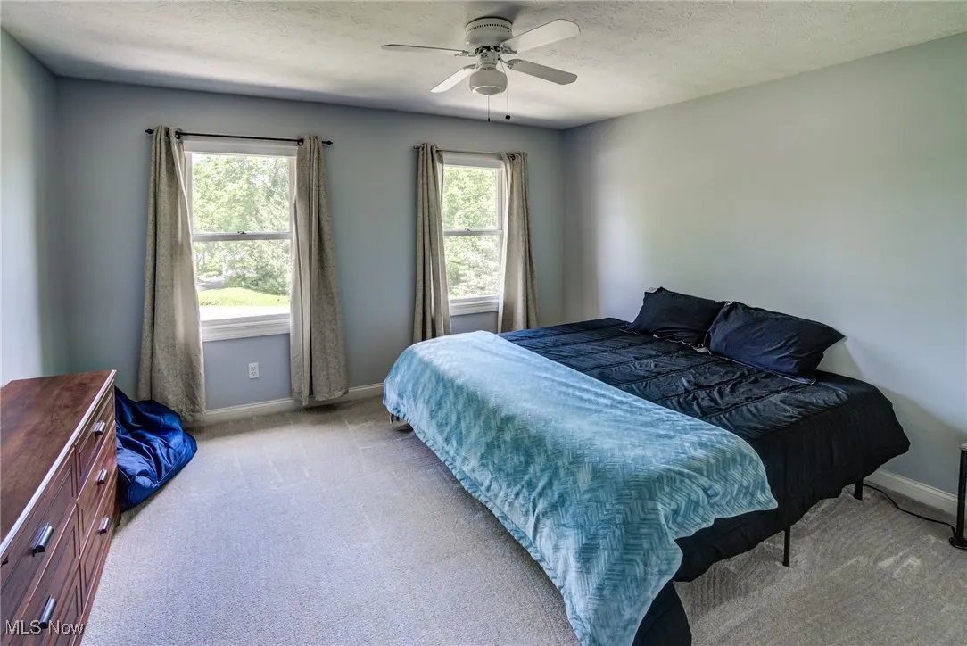 Carpeted bedroom featuring multiple windows, a textured ceiling, and a ceiling fan