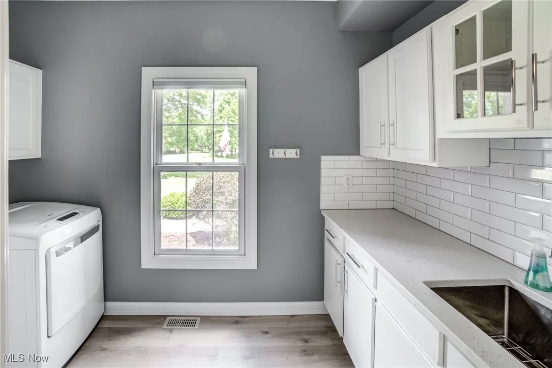 Laundry area with washer / clothes dryer, cabinet space, healthy amount of natural light, and light wood finished floors