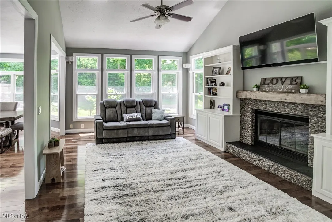 Living area featuring ceiling fan, dark wood-style floors, a high end fireplace, and high vaulted ceiling