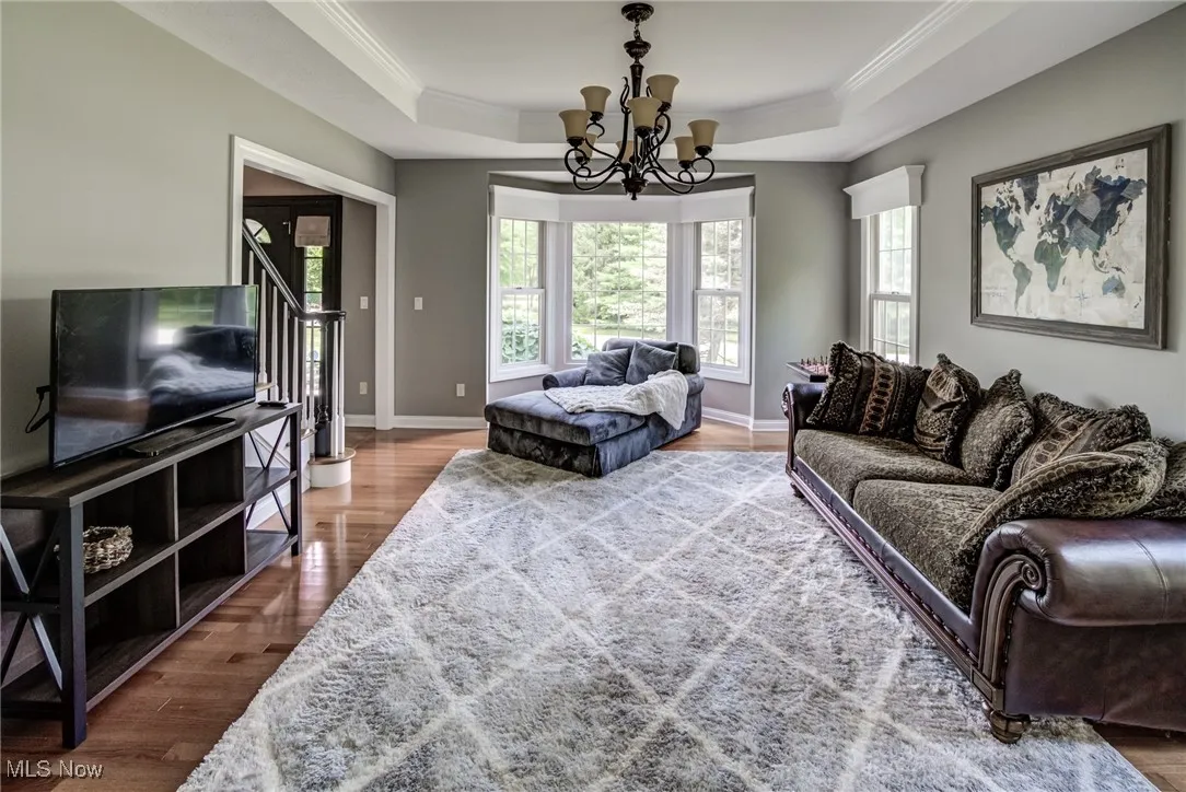 Living room featuring a tray ceiling, crown molding, wood finished floors, a chandelier, and healthy amount of natural light