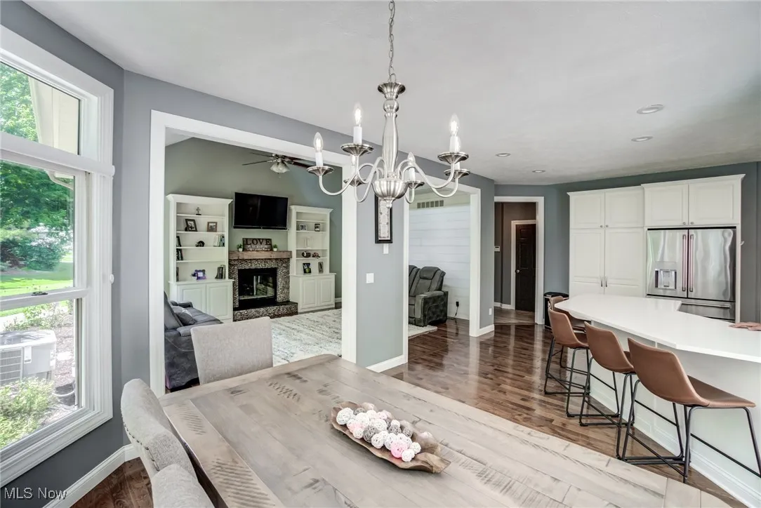 Dining room with a chandelier, a fireplace, wood finished floors, and a ceiling fan